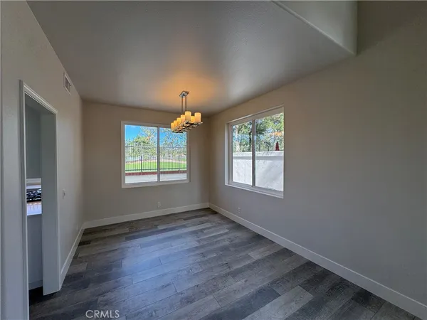 an empty room with wooden floor chandelier and windows