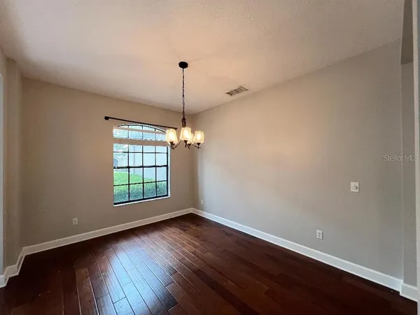 an empty room with wooden floor chandelier and windows