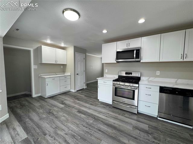 4420 Galley Road Colorado Springs, CO 80915 - Photo 8 of 20 Kitchen featuring appliances with stainless steel finishes, dark wood-type flooring, baseboards, white cabinets, and recessed lighting