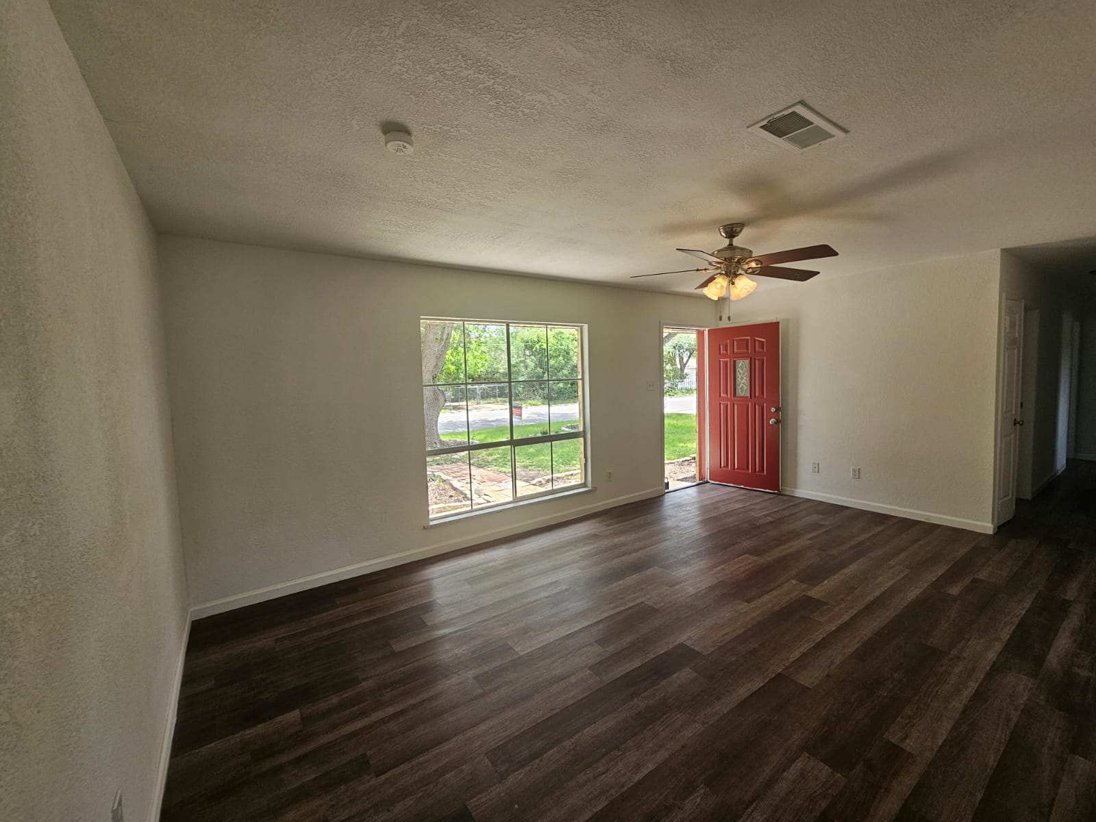 1401 Trinity Street Lockhart, TX 78644 - Photo 5 of 31 Spacious room featuring wood-finish flooring, a contemporary ceiling fan with integrated lighting, and a vibrant red entry door