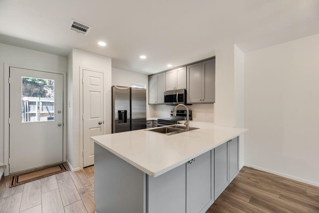 28 Abbey Road Euless, TX 76039 - Photo 3 of 19 Modern kitchen featuring gray shaker cabinetry, stainless steel appliances, a white solid-surface countertop island with an undermount double sink, recessed lighting, and wood-finish flooring