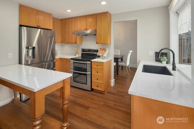 a kitchen with stainless steel appliances a stove a refrigerator a sink a dining table and chairs