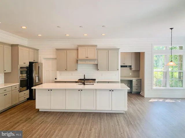 a kitchen with stainless steel appliances a stove top oven a refrigerator a sink and white cabinets with wooden floor