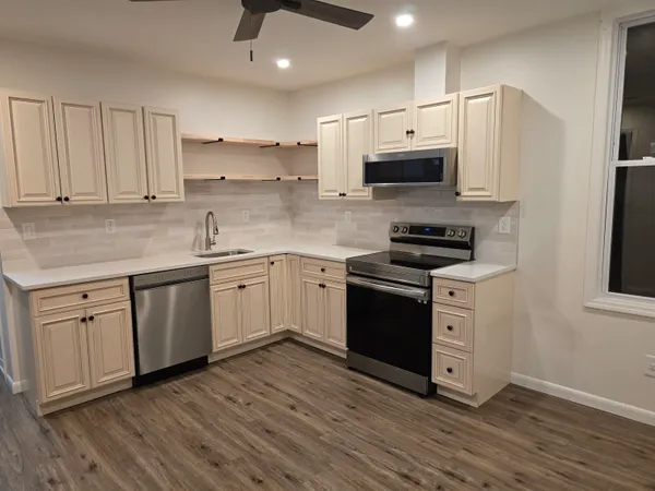 a kitchen with stainless steel appliances white cabinets a sink a stove a microwave and wooden floors