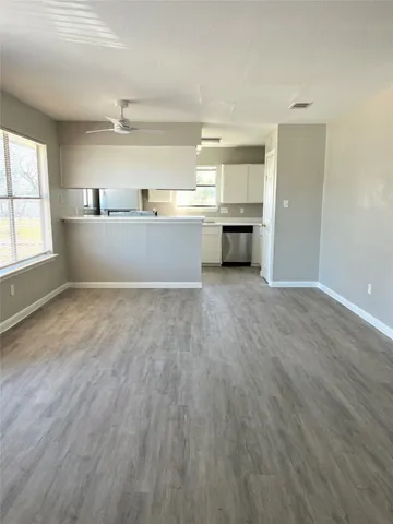 an empty room with wooden floor kitchen view and windows
