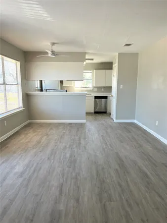 an empty room with wooden floor kitchen view and windows