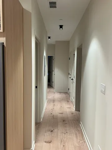 a view of a hallway with wooden floor and a bathroom