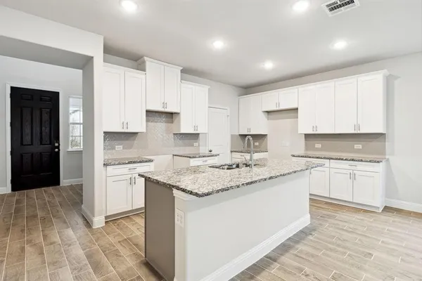 a kitchen with stainless steel appliances granite countertop a stove top oven a sink a refrigerator and white cabinets with wooden floor