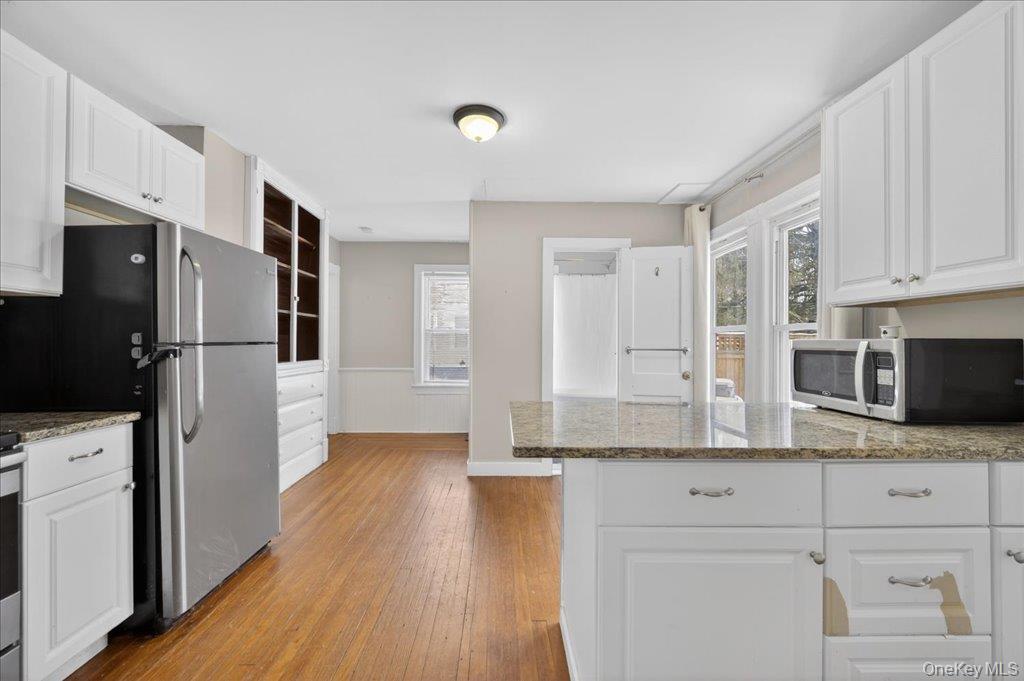 792 Springtown Road Rosendale, NY 12486 - Photo 27 of 45 Kitchen with white cabinetry, light stone countertops, stainless steel microwave, a peninsula, and wainscoting