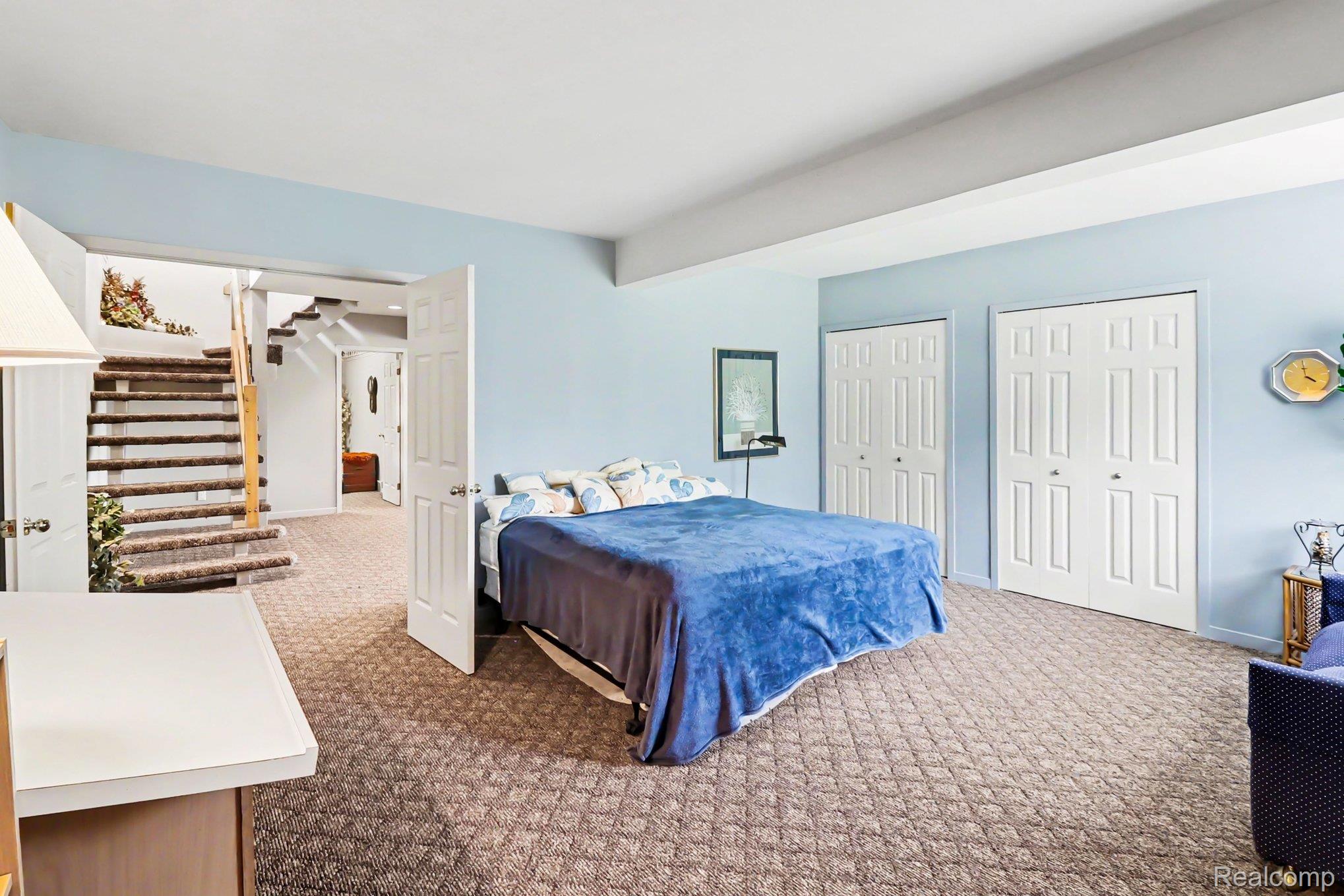18501 Taylor Lake Road Holly, MI 48442 - Photo 25 of 35 Expansive carpeted bedroom featuring light blue walls, two six-panel bifold closet doors, egress window, and direct access to a carpeted staircase with wood handrails