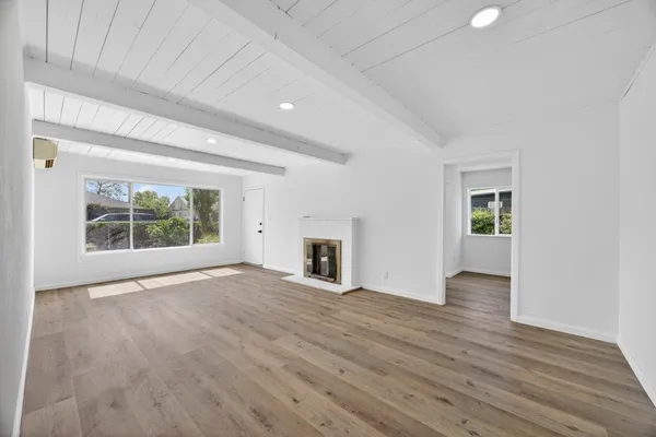 an empty room with wooden floor fireplace and windows