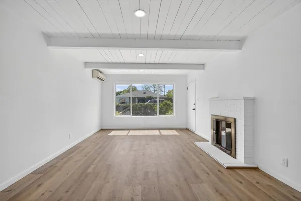 an empty room with wooden floor fireplace and windows