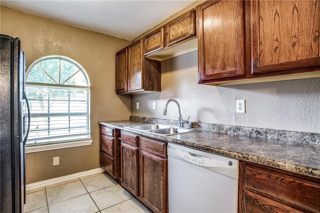 6817 Haltom Road Fort Worth, TX 76137 - Photo 19 of 25 Kitchen featuring rich wood cabinetry, patterned countertops, a double basin sink with a gooseneck faucet, an arched window, and tile flooring
