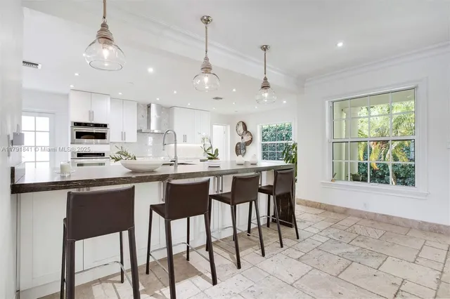 a kitchen with stainless steel appliances granite countertop a sink a stove a dining table and chairs with white cabinets