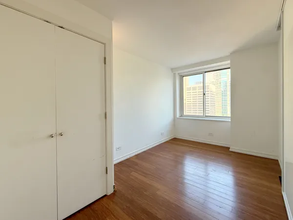 an empty room with wooden floor closet and windows