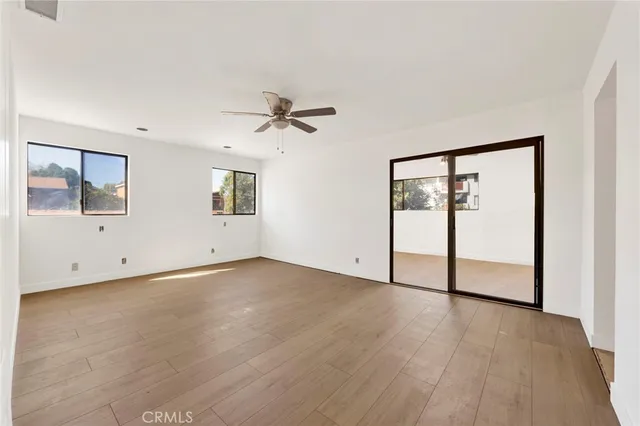 a view of an empty room with wooden floor and a ceiling fan