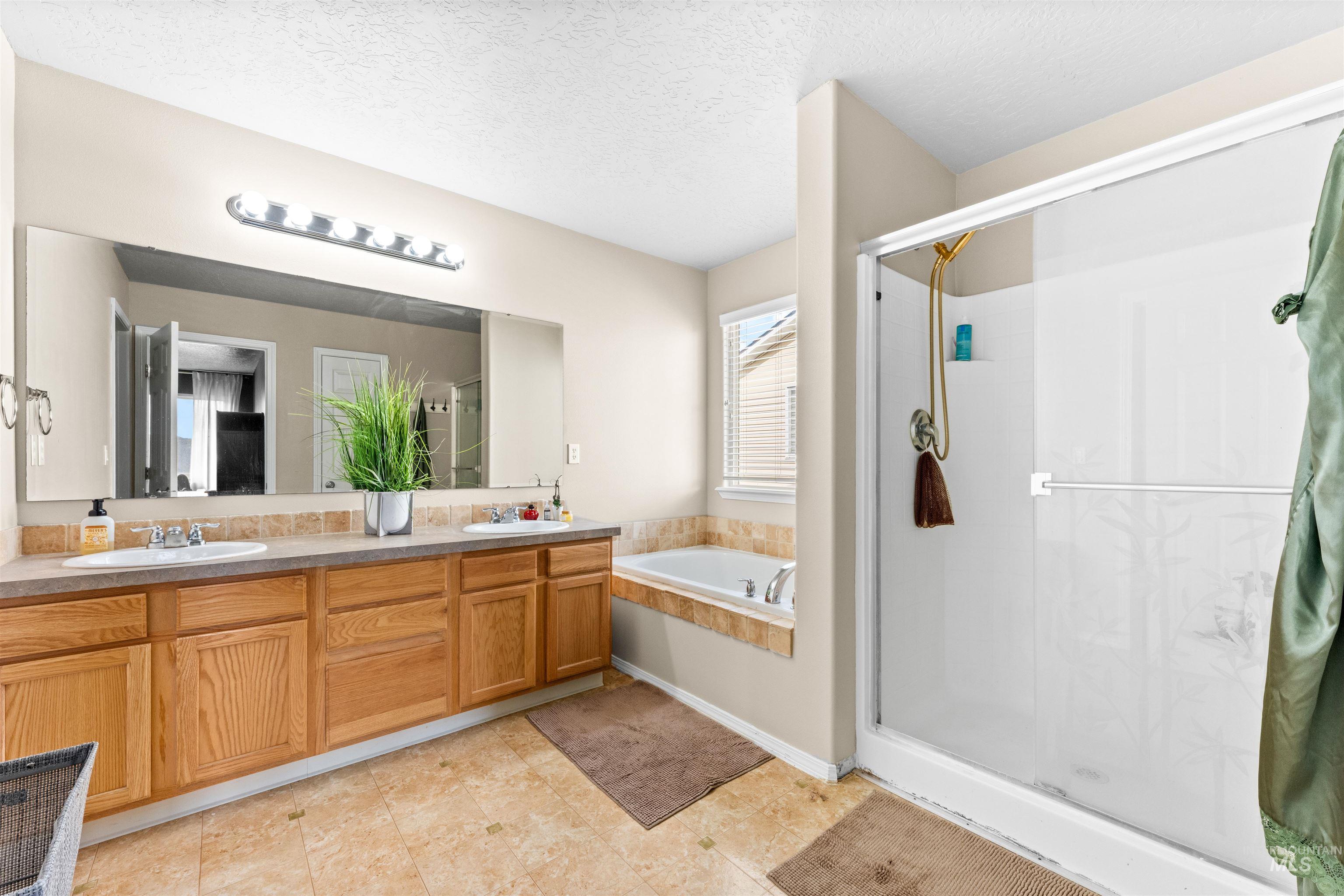 5021 Lathrop Place Caldwell, ID 83607 - Photo 24 of 43 Full bathroom with double vanity, a shower stall, a bath, and a textured ceiling