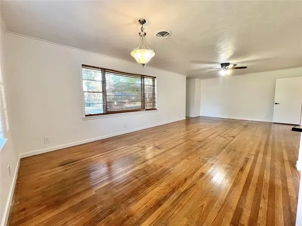 an empty room with wooden floor chandelier fan and windows