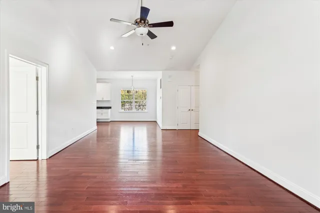 a view of an empty room with wooden floor and a ceiling fan