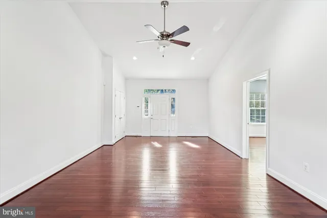 an empty room with wooden floor ceiling fan and windows