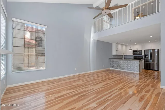 a view of an empty room with wooden floor and a kitchen