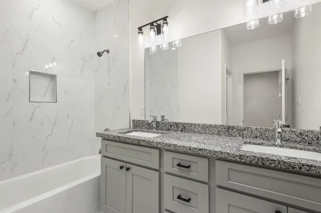 a bathroom with a granite countertop sink two mirror and a bathtub
