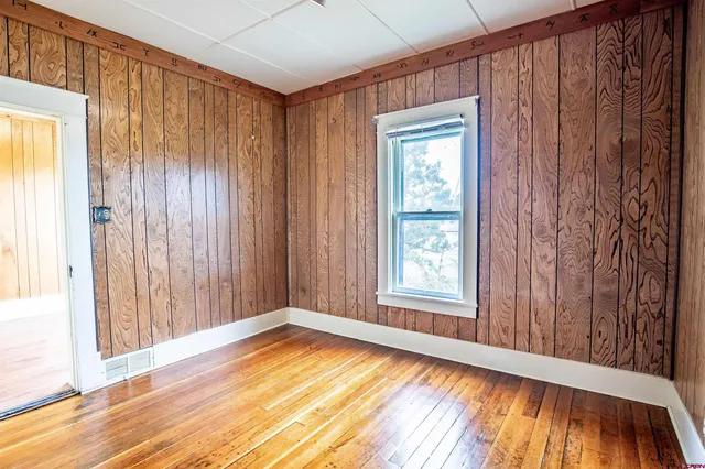 an empty room with wooden floor and windows with curtains