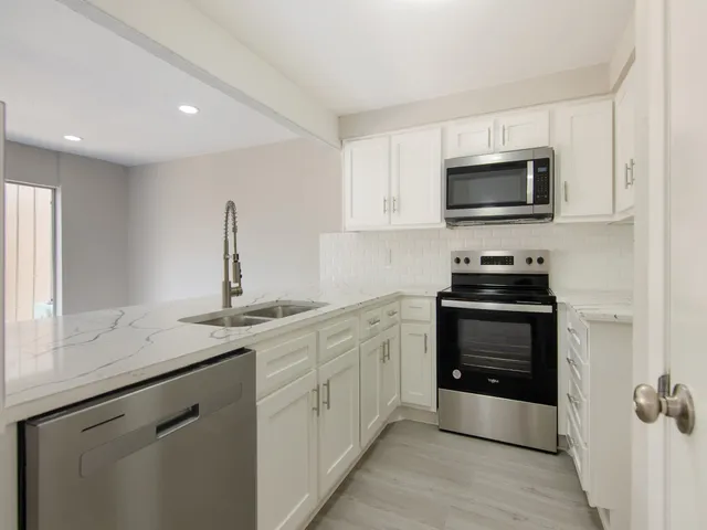 a kitchen with stainless steel appliances granite countertop white cabinets a sink and a window