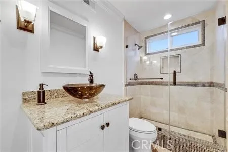 a bathroom with a granite countertop sink a toilet a mirror and shower