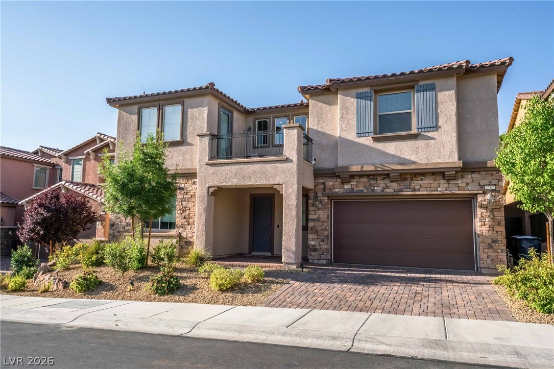 2787 Athens Ridge Drive Henderson, NV 89052 - Photo 2 of 31 A warm facade features stone accents, a second-story balcony, and a paver driveway leading to the garage.