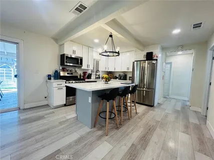 a kitchen with stainless steel appliances a refrigerator a stove a sink dishwasher a dining table and chairs with wooden floor