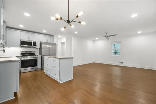 a view of an empty room with wooden floor and a kitchen