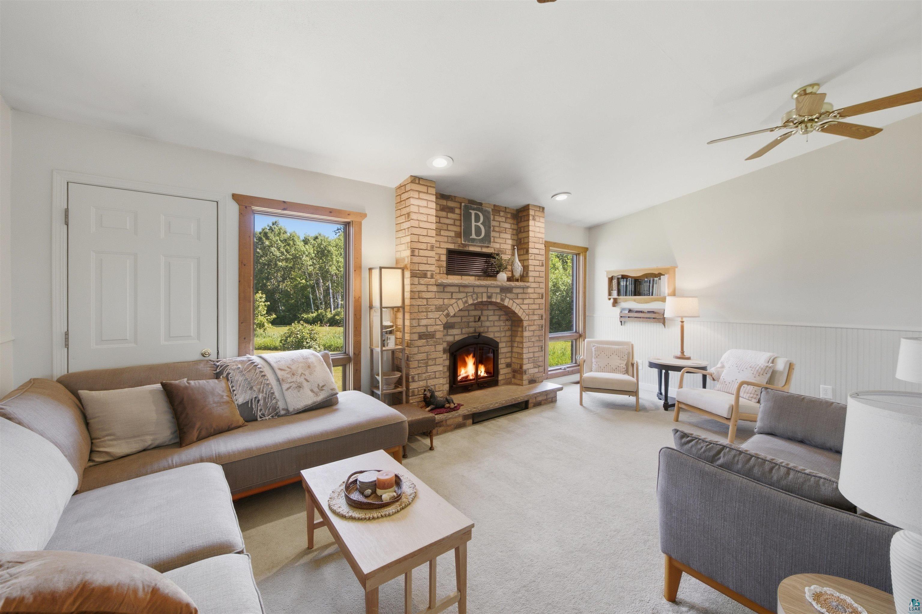 64260 Jolma Road Ashland, WI 54806 - Photo 12 of 35 Living room featuring a brick fireplace with hearth, wood-trimmed windows, and white beadboard wall accents