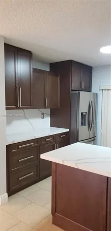 a kitchen with stainless steel appliances kitchen island granite countertop a refrigerator a stove and a sink with wooden cabinets