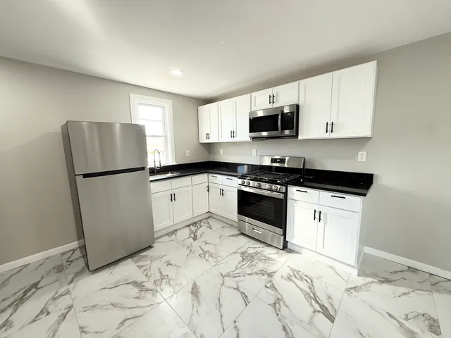a kitchen with granite countertop a refrigerator sink and white cabinets