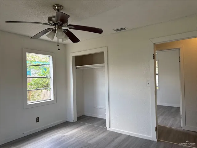 a view of an empty room with wooden floor and a ceiling fan