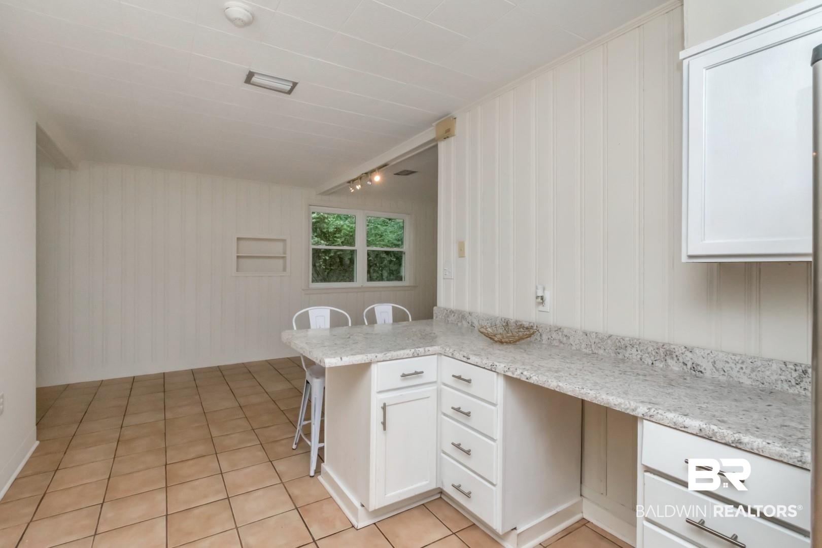 1906 Old Shell Road Mobile, AL 36607 - Photo 19 of 26 Kitchen featuring kitchen peninsula, white cabinets, light stone countertops, light tile patterned floors, and a kitchen breakfast bar