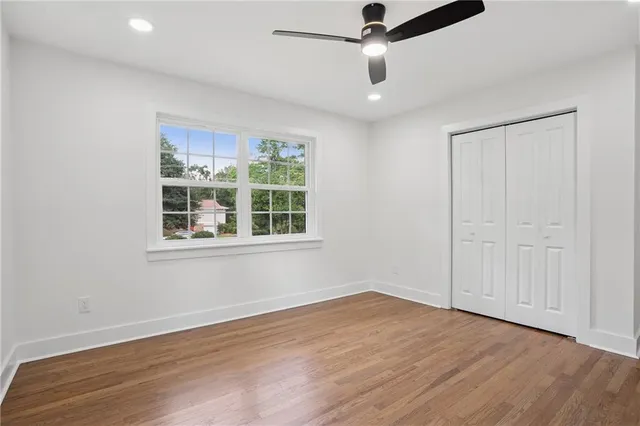 an empty room with wooden floor chandelier fan and windows