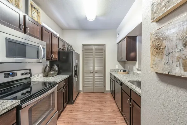 a kitchen with stainless steel appliances a stove top oven a sink a refrigerator white cabinets and wooden floor