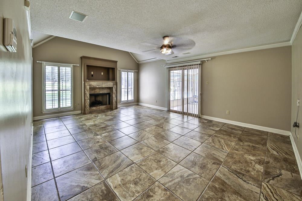 3693 Brunswick Road Bartlett, TN 38133 - Photo 19 of 30 Unfurnished living room featuring a tiled fireplace, crown molding, lofted ceiling, tile patterned floors, and ceiling fan