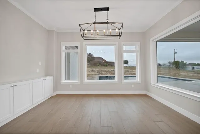 an empty room with wooden floor a chandelier and windows