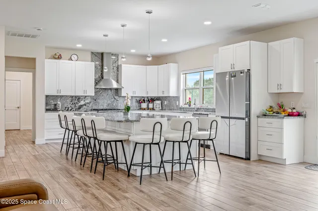 a kitchen with stainless steel appliances granite countertop a stove a refrigerator a microwave a sink and white cabinets with wooden floor