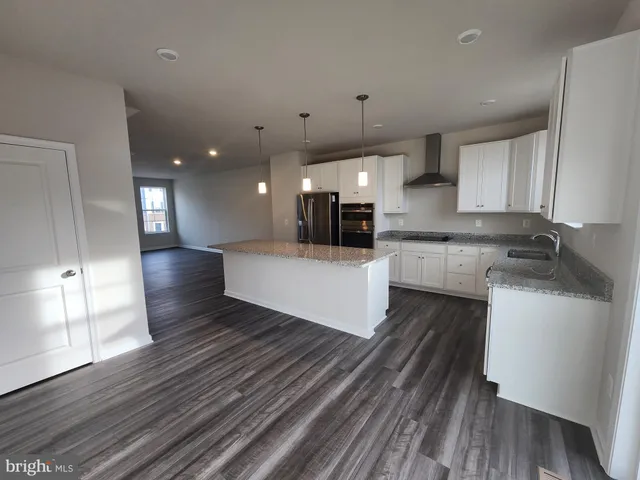a large kitchen with stainless steel appliances a large counter top a wooden floors and a view of living room