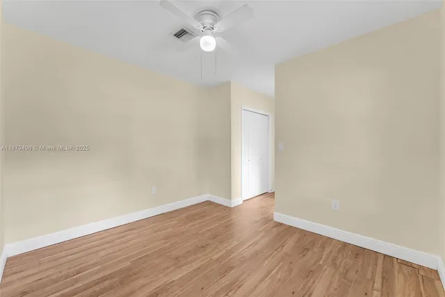 an empty room with wooden floor and fan