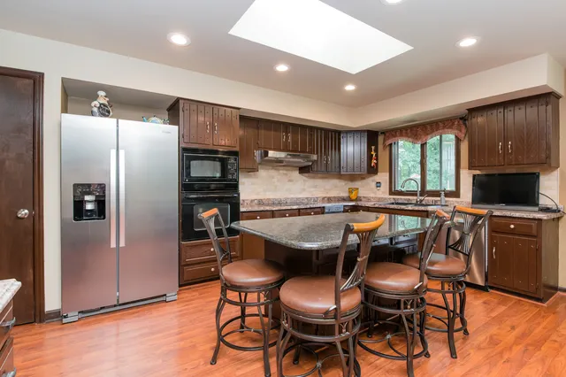 a kitchen with stainless steel appliances granite countertop a refrigerator a sink dishwasher a stove and a refrigerator with wooden floor