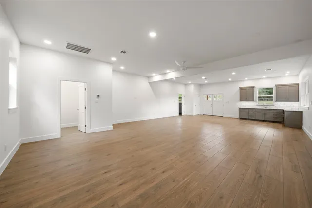 a view of an empty room and a kitchen with wooden floor