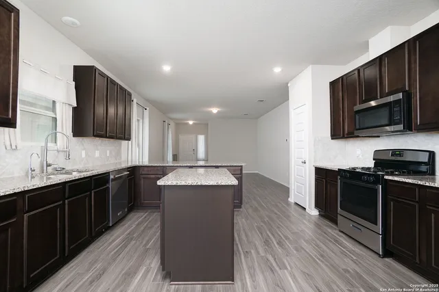 a kitchen with stainless steel appliances granite countertop wooden cabinets a refrigerator a stove a sink and dishwasher with wooden floor