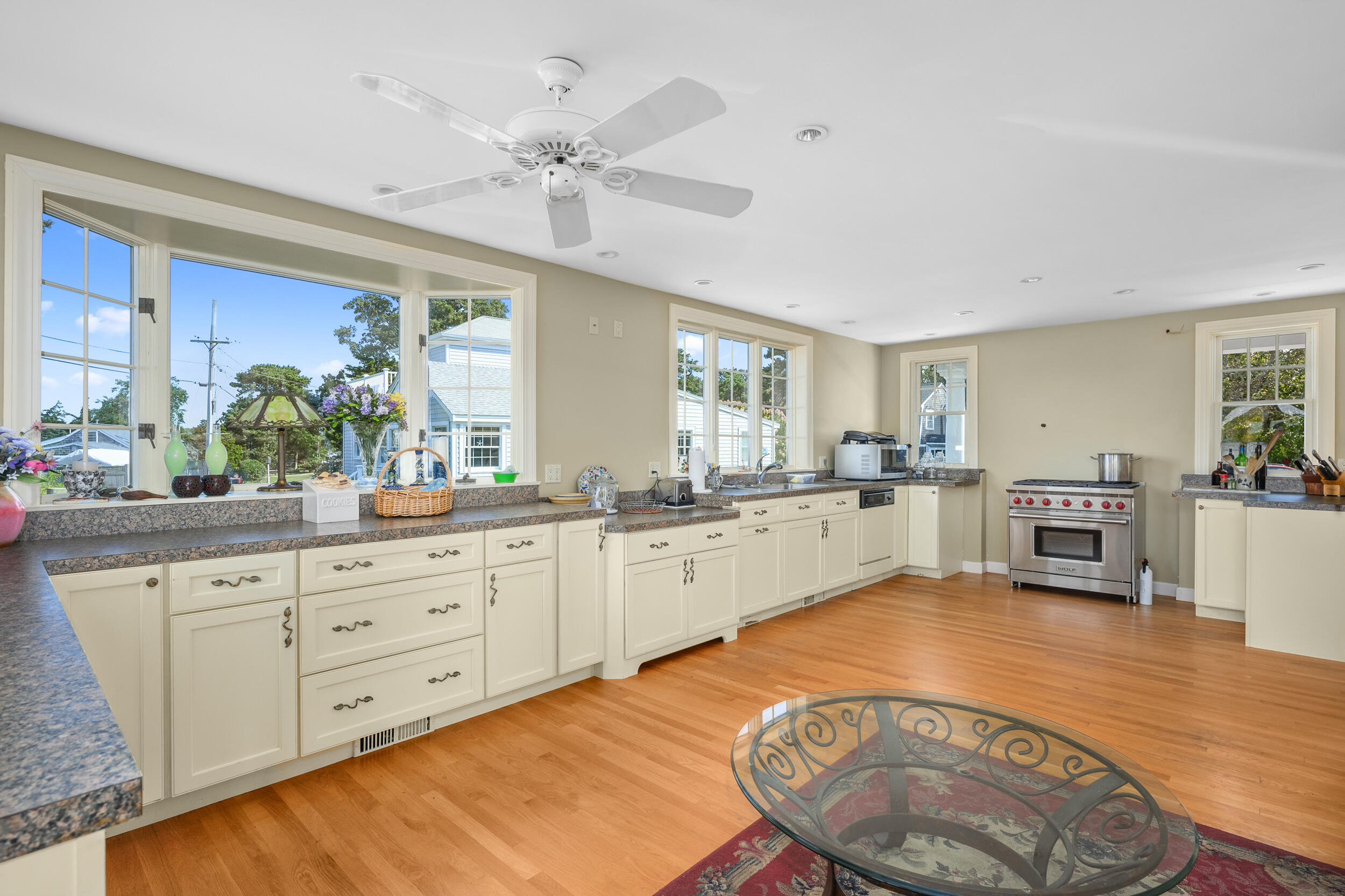 27 Mayflower Lane Dennis Port, MA 02639 - Photo 24 of 35 a large white kitchen with kitchen island a stove a sink a dining table and chairs with wooden floors