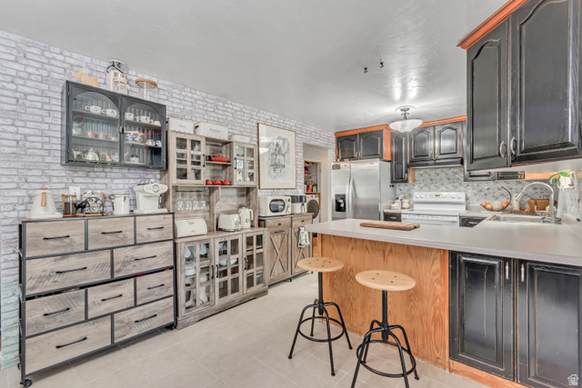 7470 Ramanee Drive Midvale, UT 84047 - Photo 9 of 29 Kitchen featuring a peninsula, light countertops, stainless steel refrigerator with ice dispenser, white electric stove, and a kitchen breakfast bar