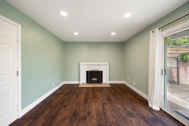 a view of an empty room with wooden floor fireplace and a window